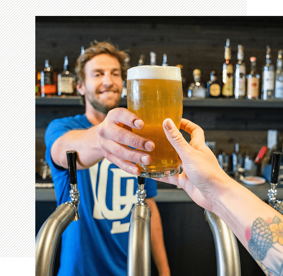 A man and woman holding beers at a bar.